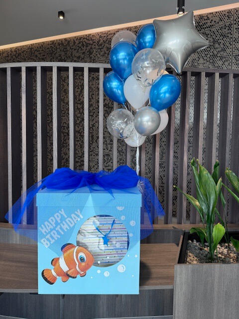 Nemo-themed birthday gift box with blue tulle and a bunch of blue, silver and white helium balloons. "Happy Birthday" message on the front.